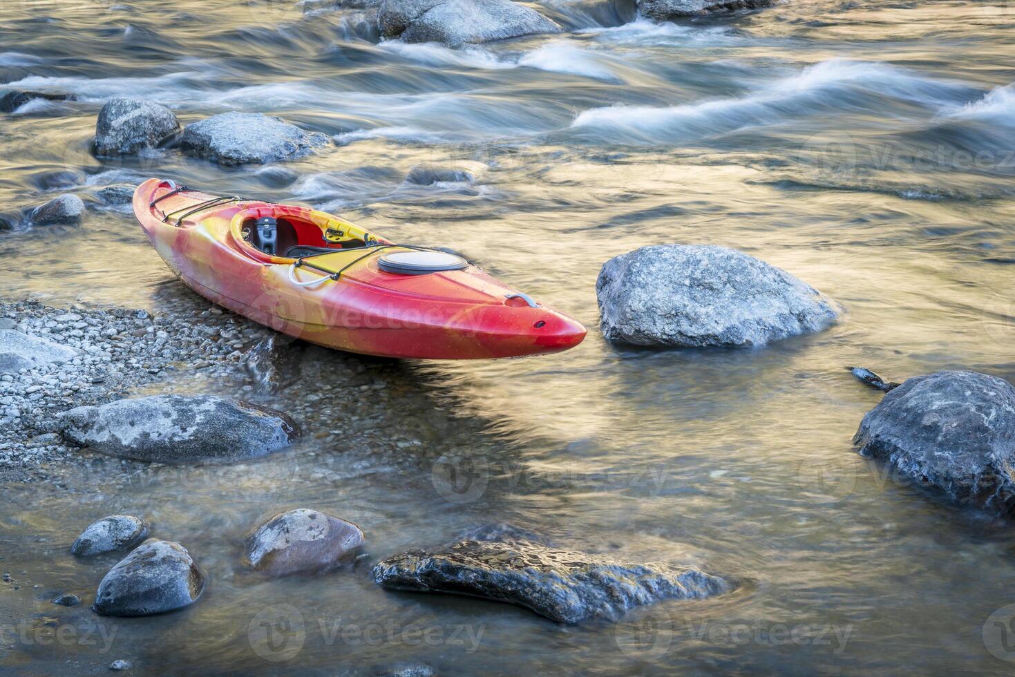 whitewater kayak on a river shore with a rapid in background photo