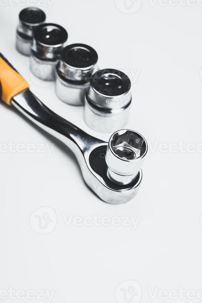 Hand tools arranged for mechanical work with a ratchet wrench and various sockets on a white surface in a well-lit environment photo
