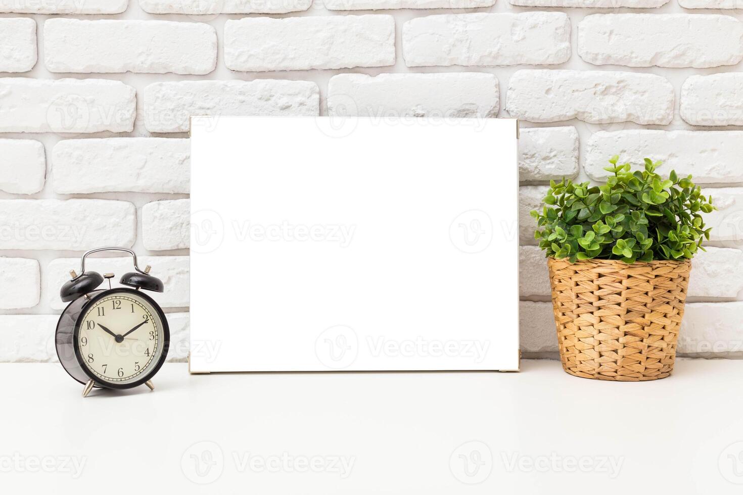 Clock and empty canvas on a table beside a green plant in a modern interior setting photo