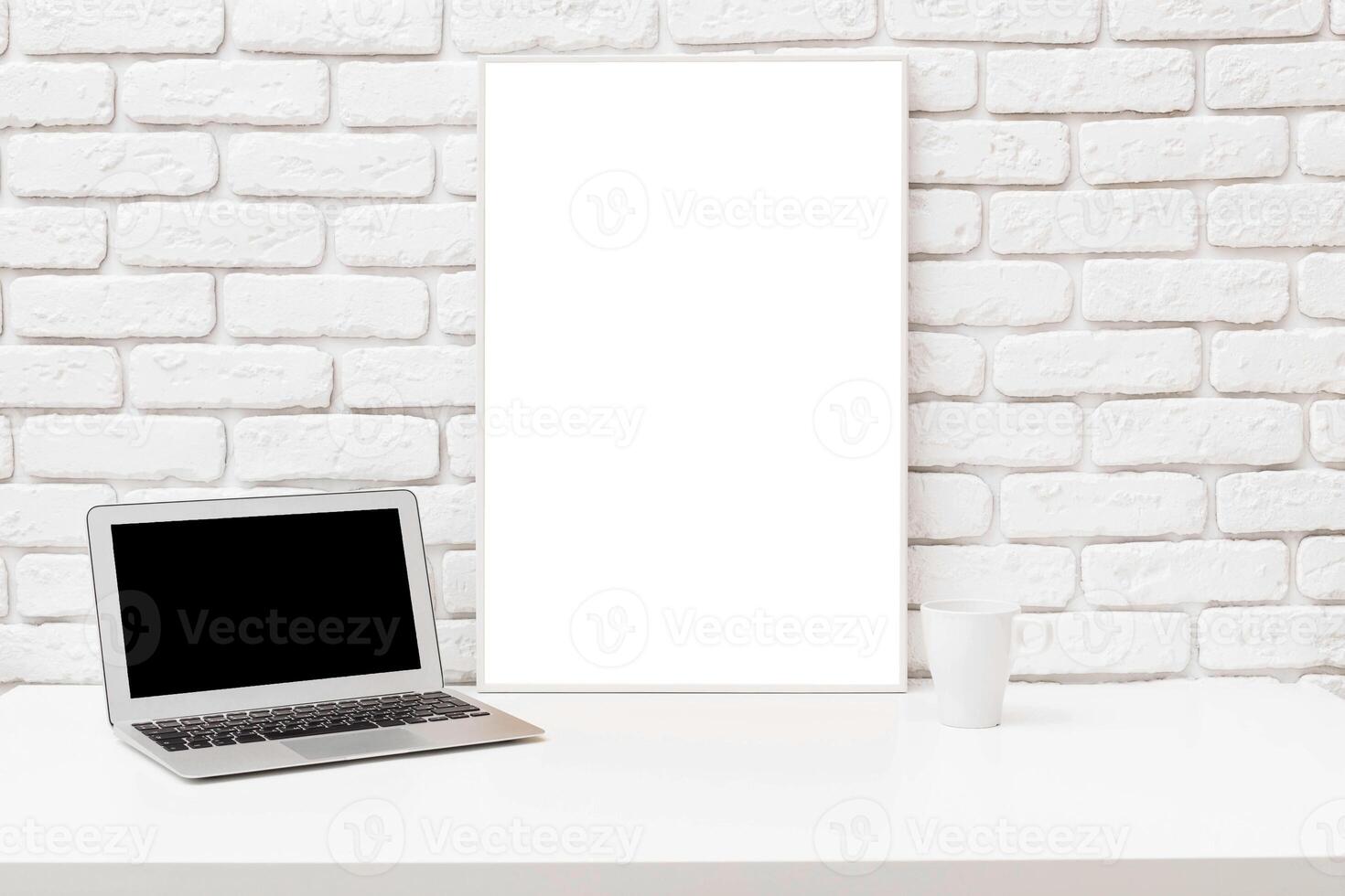 Workspace featuring a laptop and a blank canvas on a minimalist desk against a brick wall photo