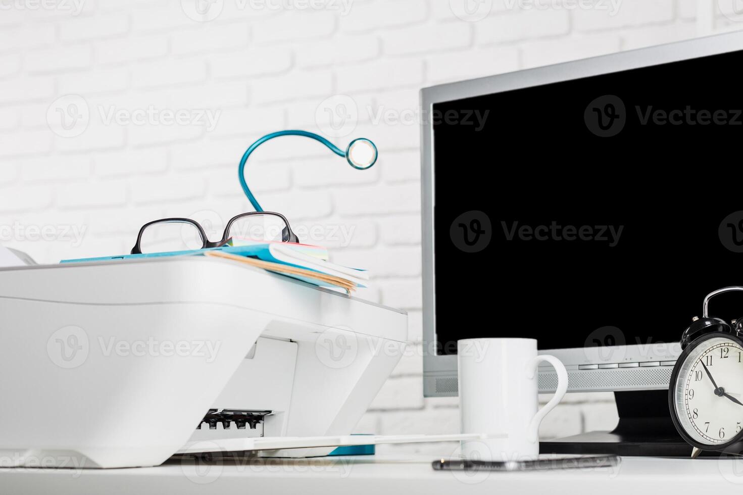 Home office workspace featuring printer, monitor, clock, and coffee cup with organized documents in a well-lit room photo