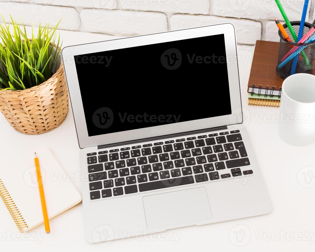 Workspace with a laptop, notebook, and cup on a desk in a bright environment photo