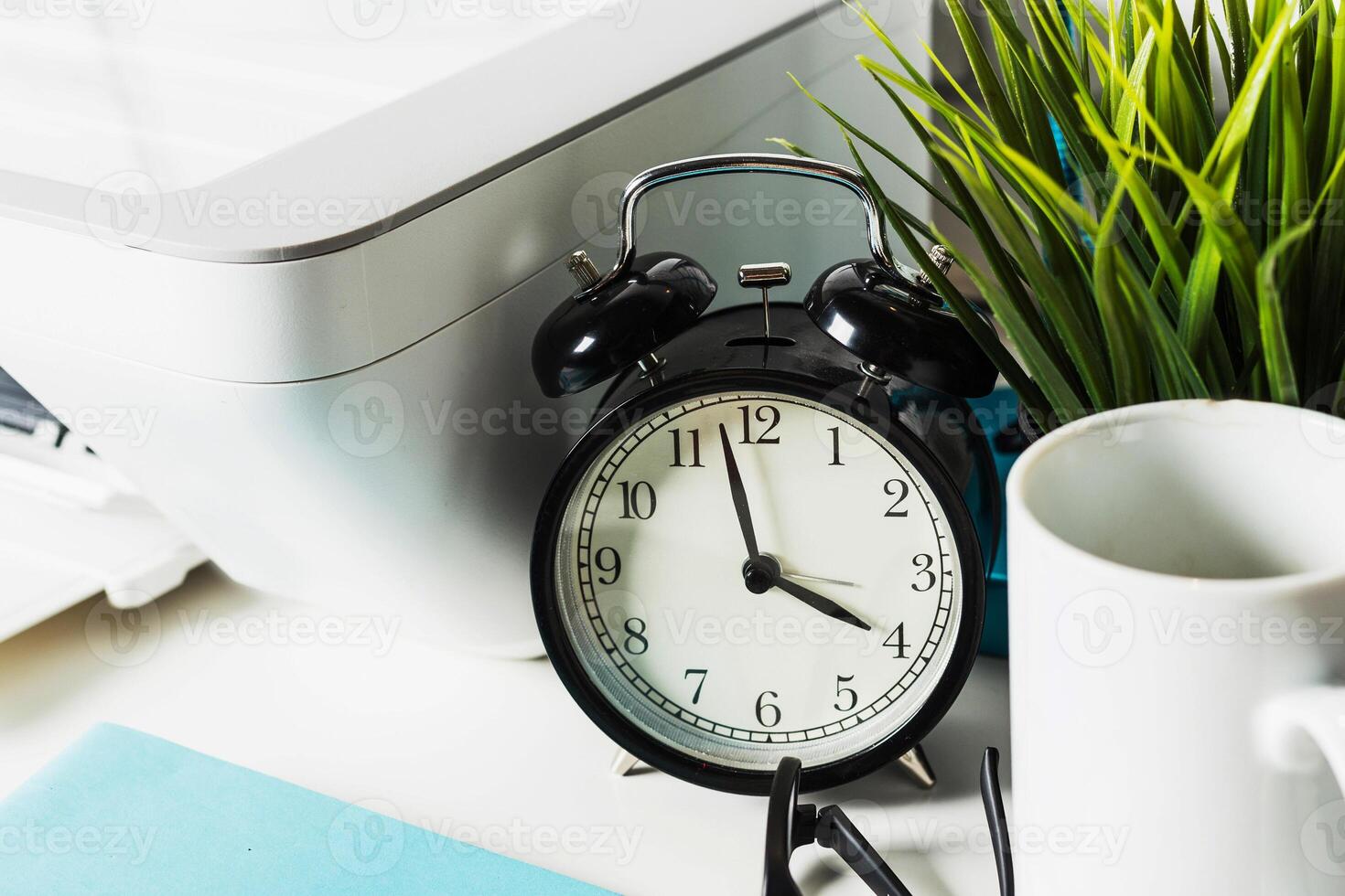 Clock placed on a desk beside a plant, printer, and mug in a workspace filled with productivity elements photo