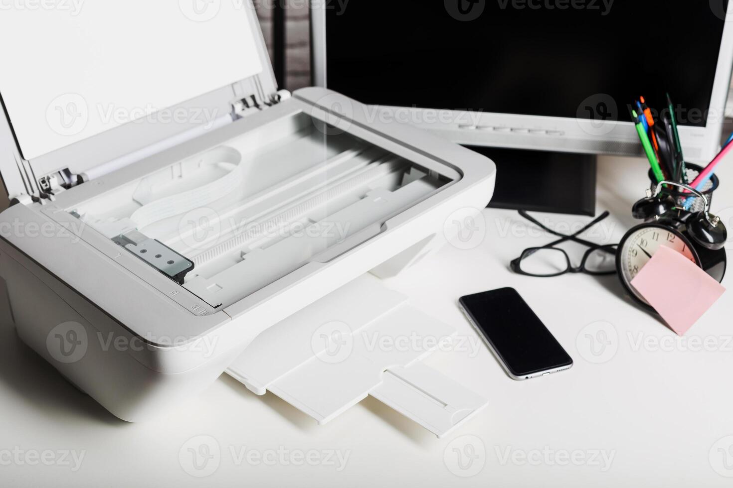 Desk setup with printer, smartphone, and clock during work hours in a modern office environment photo