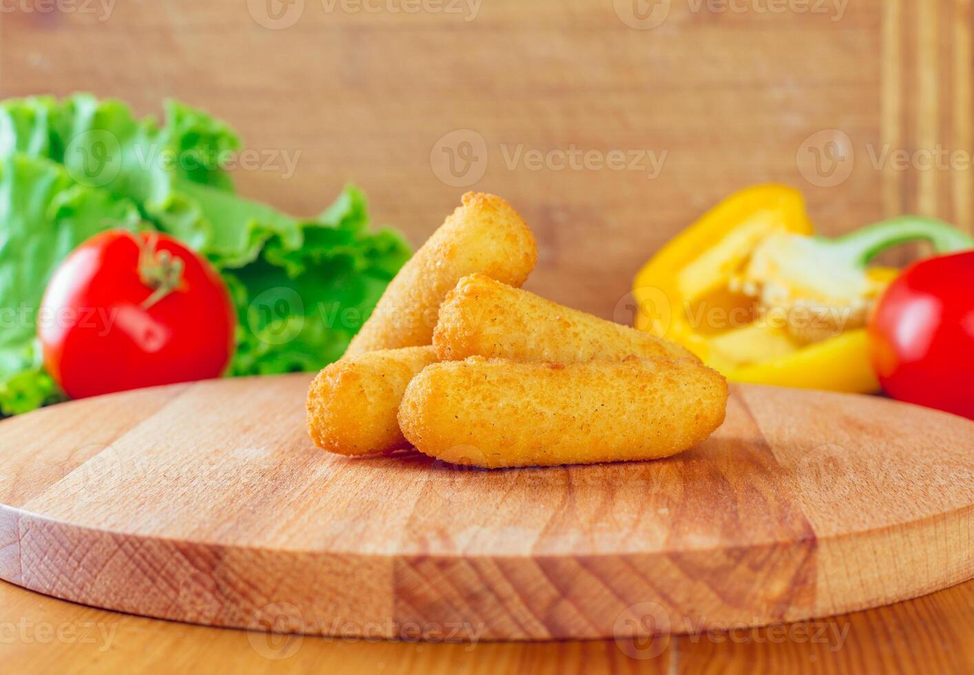 Delicious crispy croquettes on a wooden board surrounded by fresh vegetables in a cozy kitchen setting photo