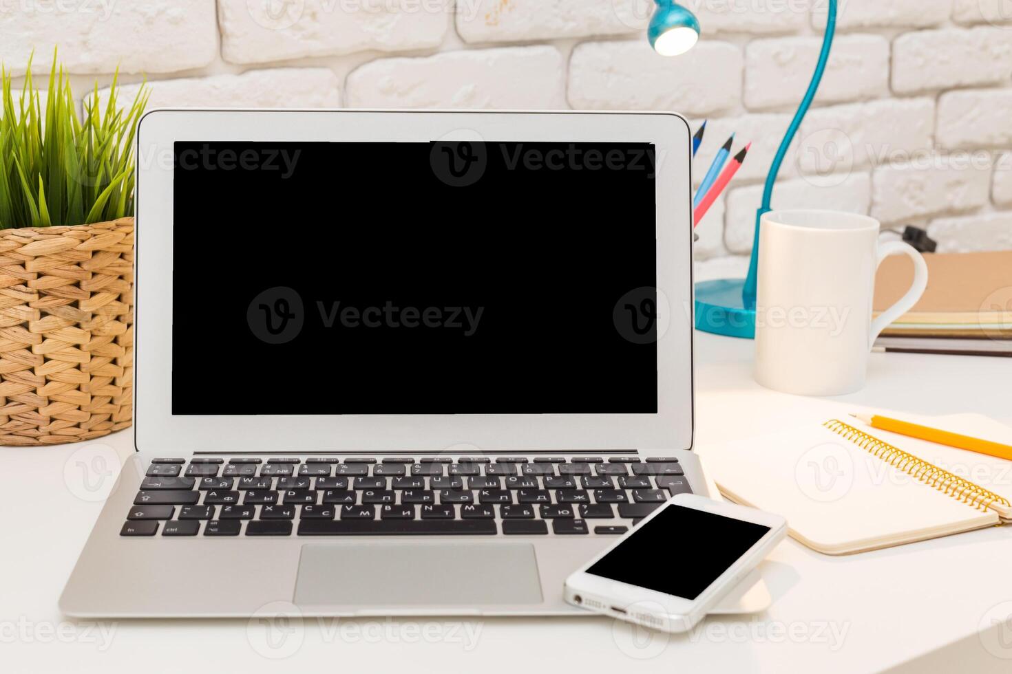 Modern workspace featuring a laptop, smartphone, and office supplies in a cozy environment with a plant and a cup photo