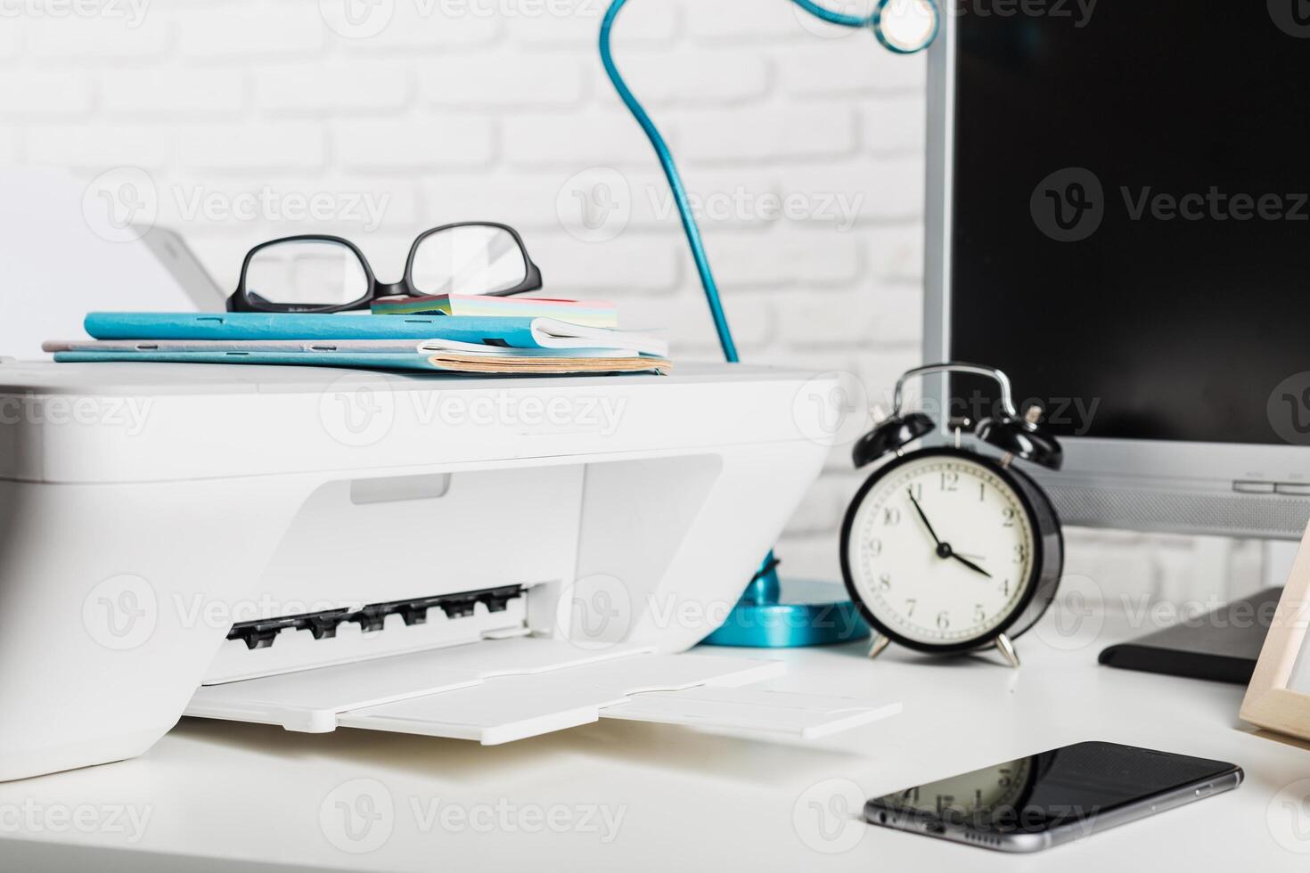 Desk setup with printer, clock, and office supplies in a bright workspace during the day photo