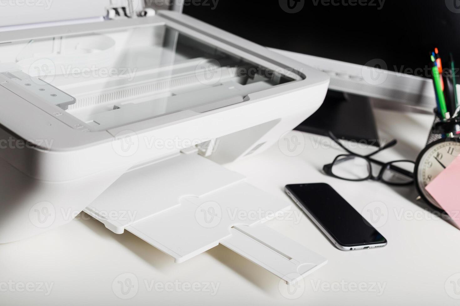Office lighting highlights a modern printer beside a smartphone and a desk clock in a productive workspace photo
