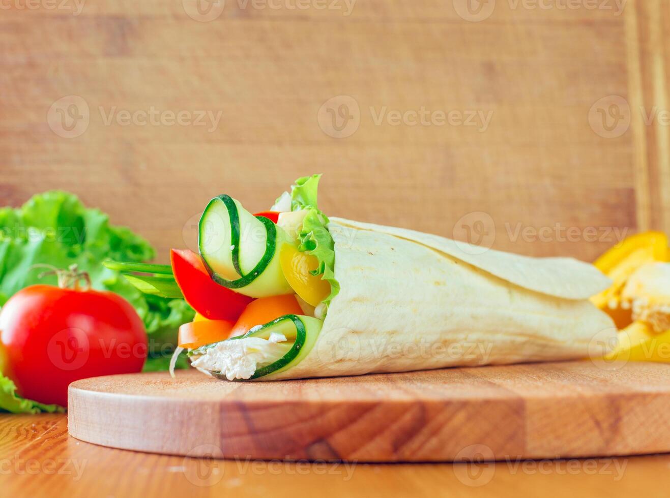 Fresh vegetable wrap on a wooden cutting board with vibrant ingredients displayed around photo