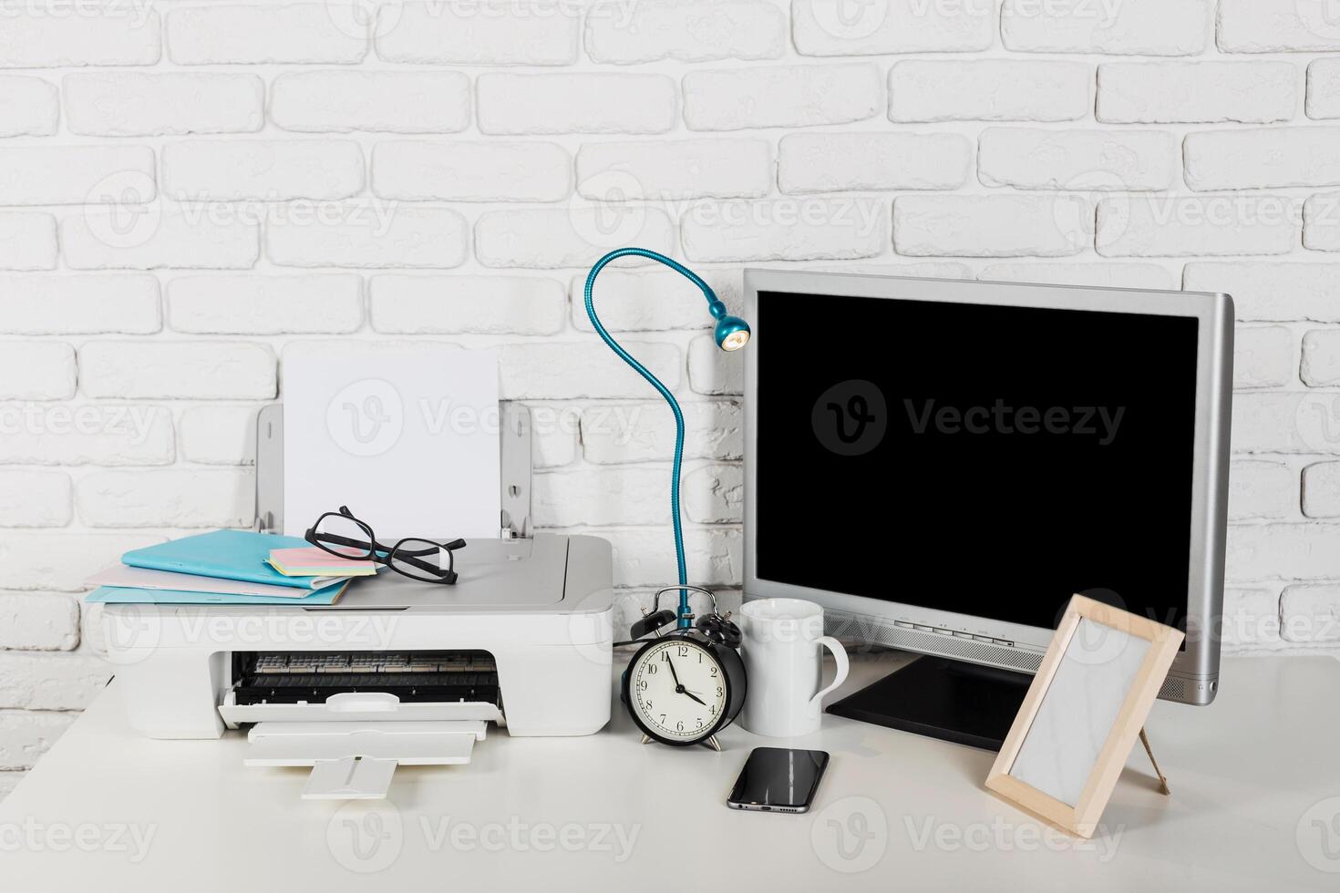 Workspace setup with printer, monitor, clock, and stationery in a modern office environment photo