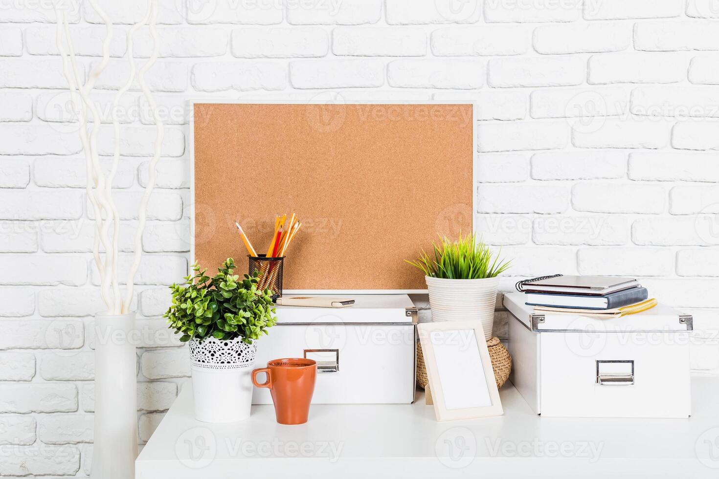 Elegant workspace with corkboard, stationery, and decorative plants against a white brick wall photo