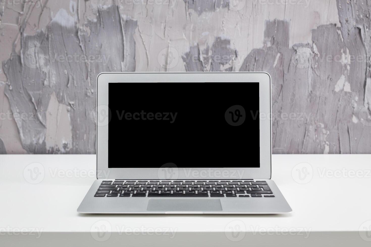 Modern laptop on a minimalist desk against a textured gray wall in a stylish office setting photo