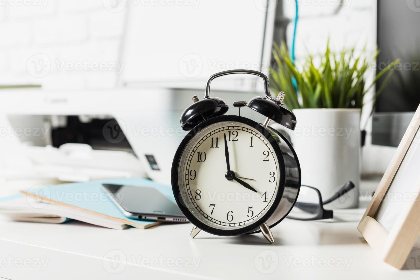 Classic black alarm clock on a modern workspace with plants and technology in a bright office environment photo