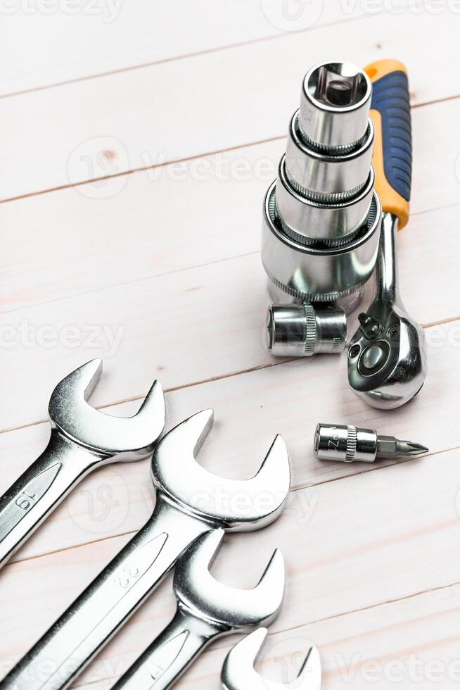 Various hand tools including wrenches and a ratchet set arranged on a wooden surface photo