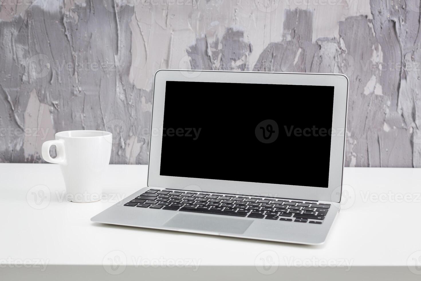 Modern workspace with laptop and coffee cup on minimalistic table against a textured wall backdrop photo