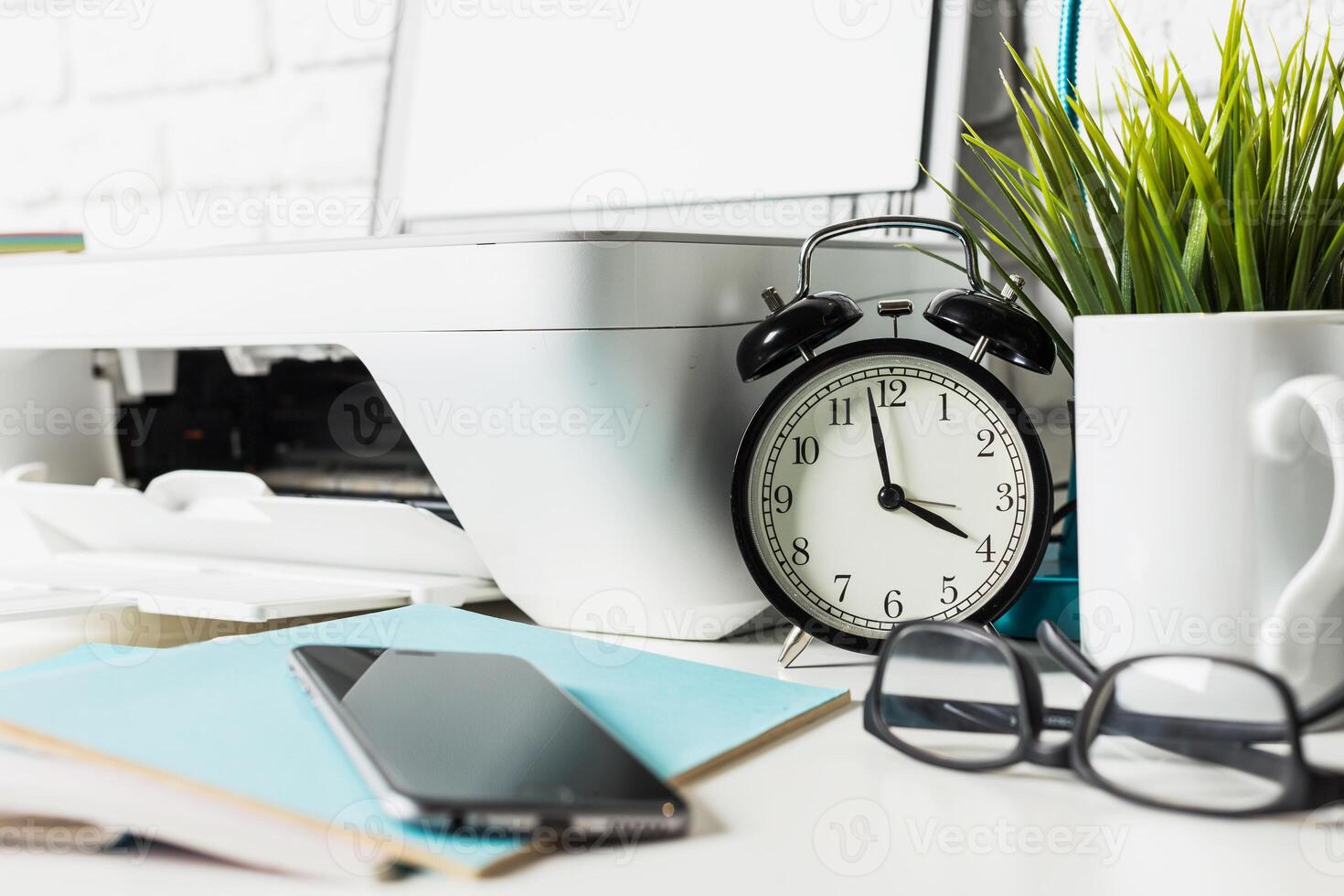 Clock and office supplies on a workspace with modern technology and greenery indicating a productive environment photo