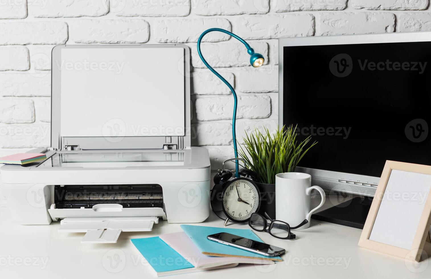 Workspace essentials showcasing printer, monitor, clock, and desk items in a modern office setting photo