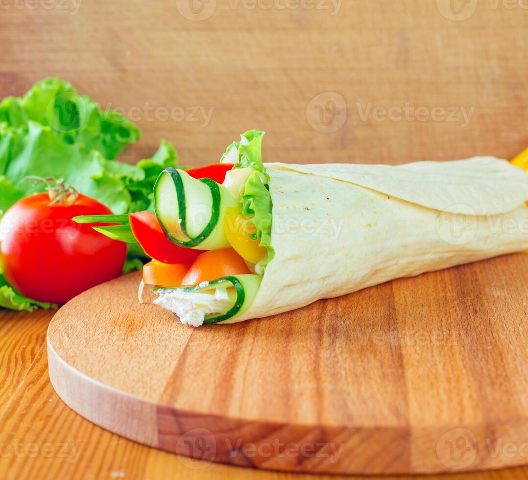 Fresh vegetable wrap with lettuce, tomato, and cucumber on a wooden cutting board photo