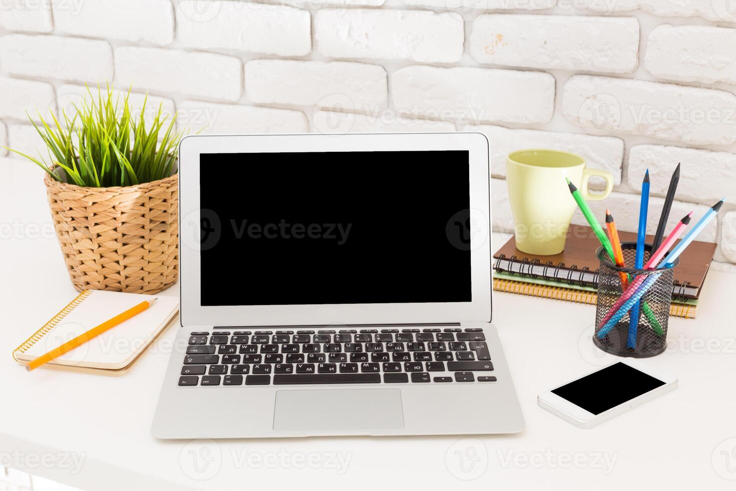 Modern workspace setup with laptop, stationery, and plants in a bright environment photo