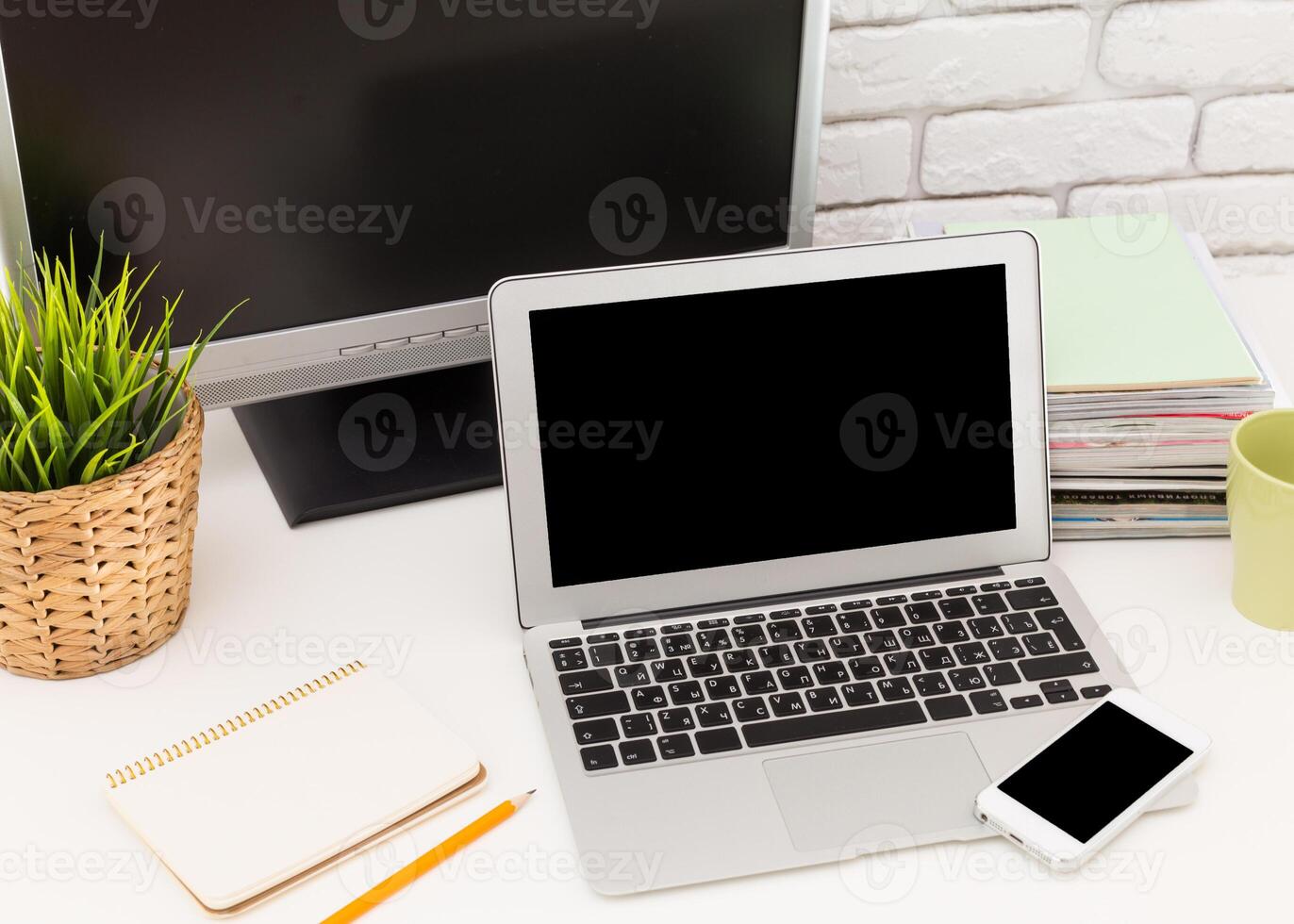 Workspace setup featuring laptop, monitor, and stationery with greenery in a modern office environment photo