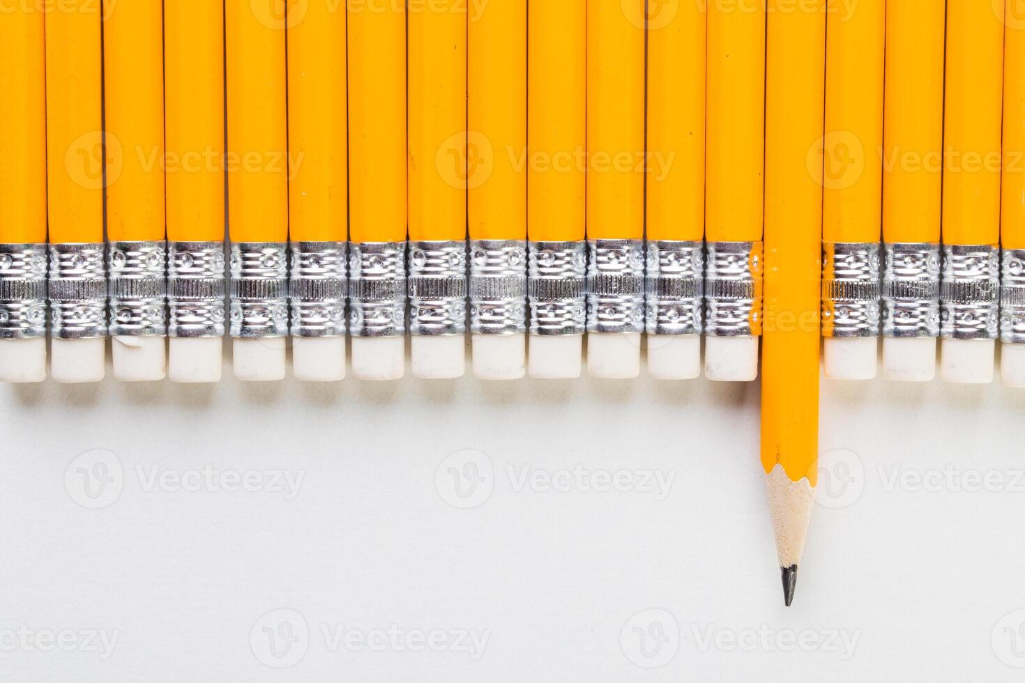 Bright yellow pencils arranged neatly with one pencil standing out on a white surface showcasing a classic school supply photo