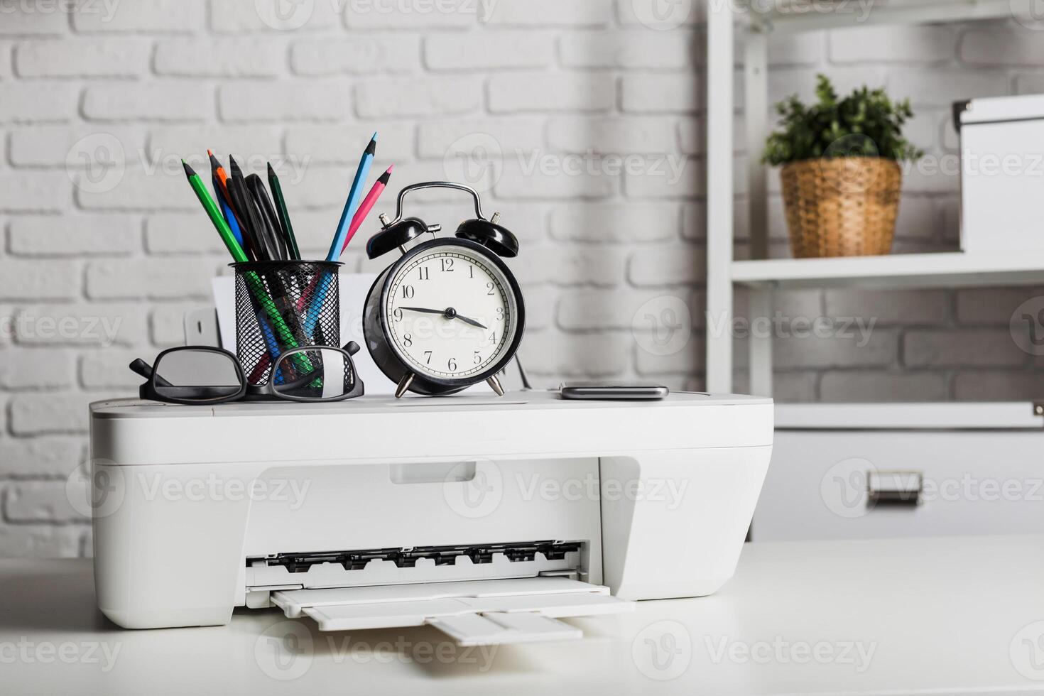 Desk setup with a printer, clock, and office supplies in a modern workspace during the day photo