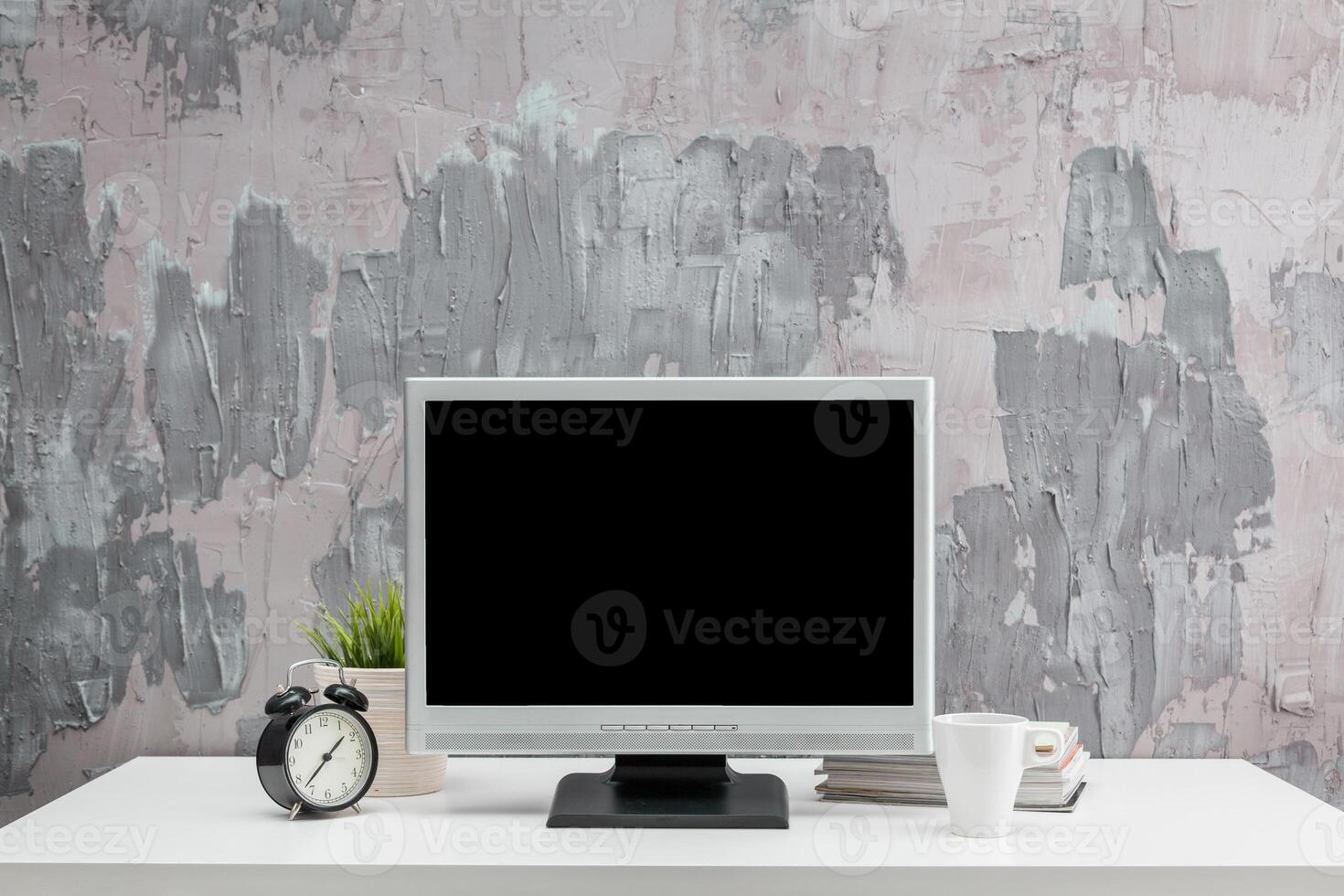Modern workspace design with a computer, clock, and coffee cup against a textured gray backdrop photo
