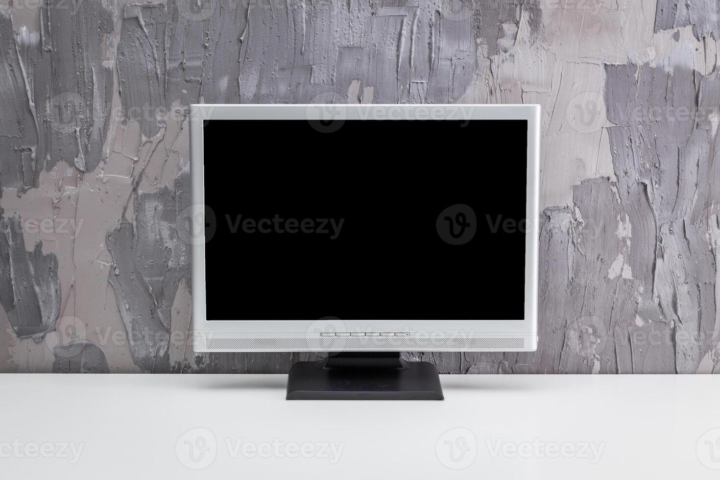 Empty desktop monitor standing on a minimalistic white table against a textured gray wall photo