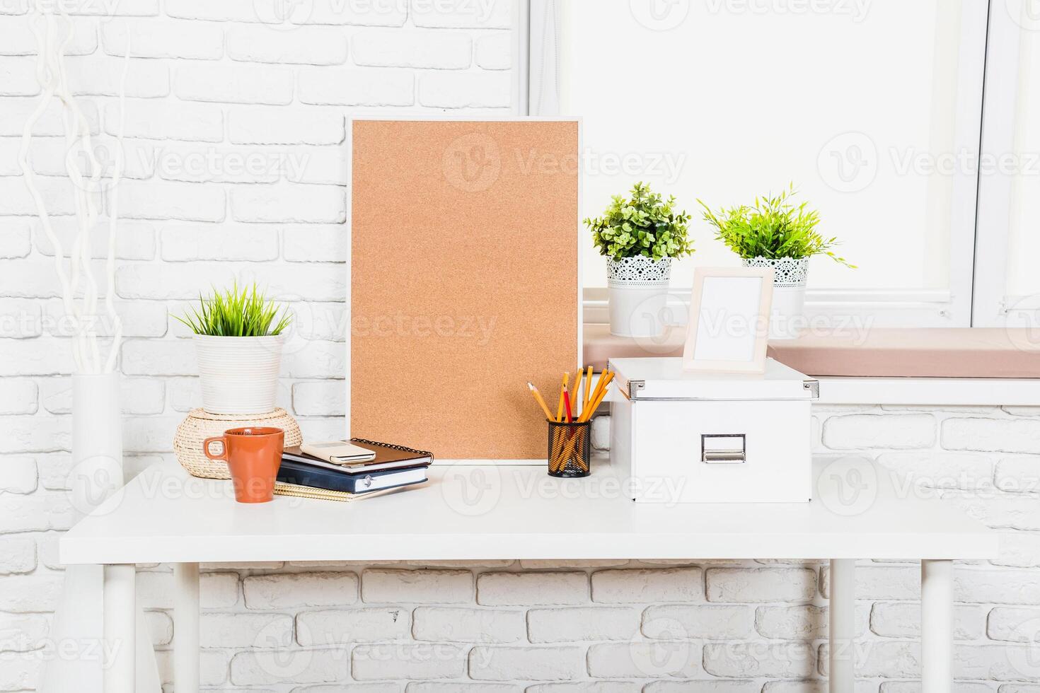 Stylish workspace design featuring plants, stationery, and a corkboard on a clean desk near a window photo