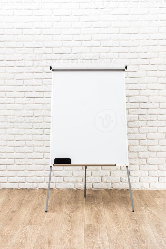 Blank flip chart on a stand in a modern interior with white brick walls and wooden floor during daylight photo