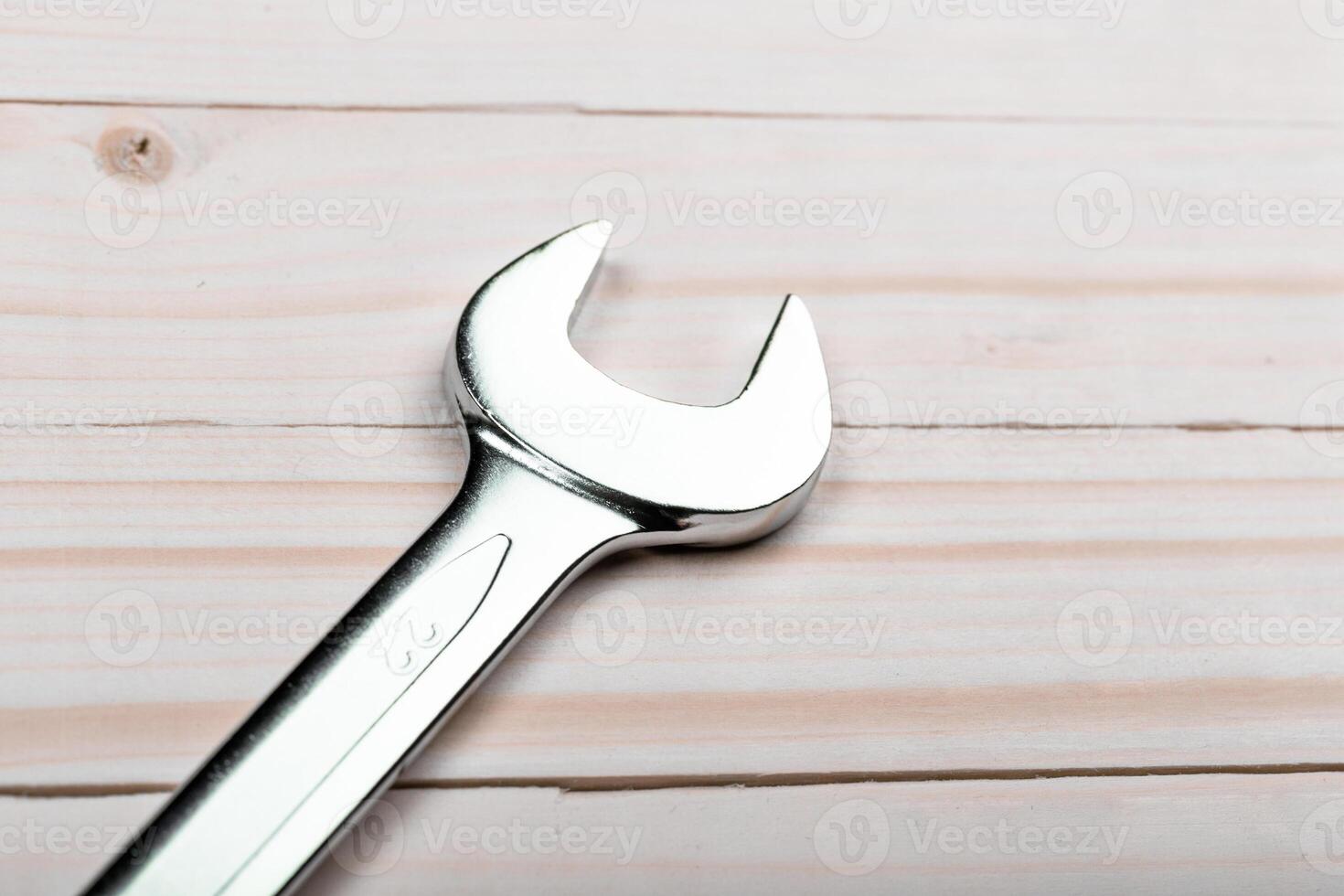 Metal wrench resting on a light wooden surface with a focus on its polished head photo