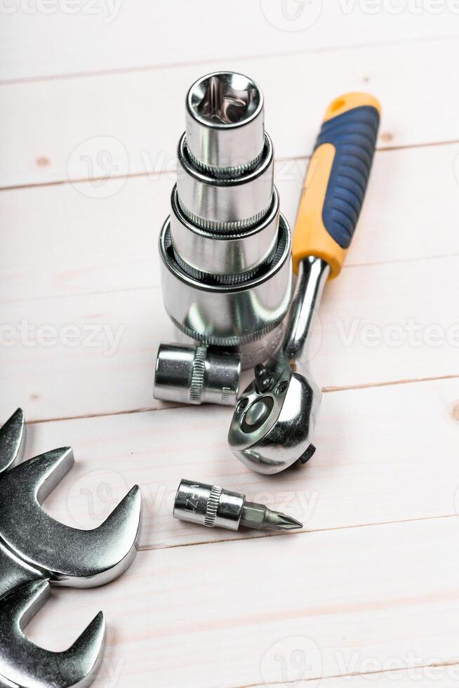 Various hand tools including sockets and a ratchet wrench arranged on a wooden surface photo