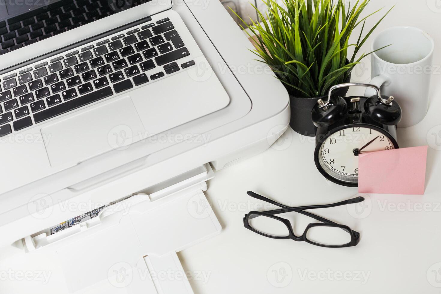 Workspace setup with laptop, clock, plants, and office supplies in a modern environment photo