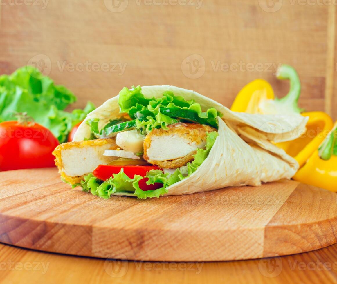 Delicious wrap filled with crispy chicken, fresh vegetables, and creamy dressing served on a wooden cutting board photo