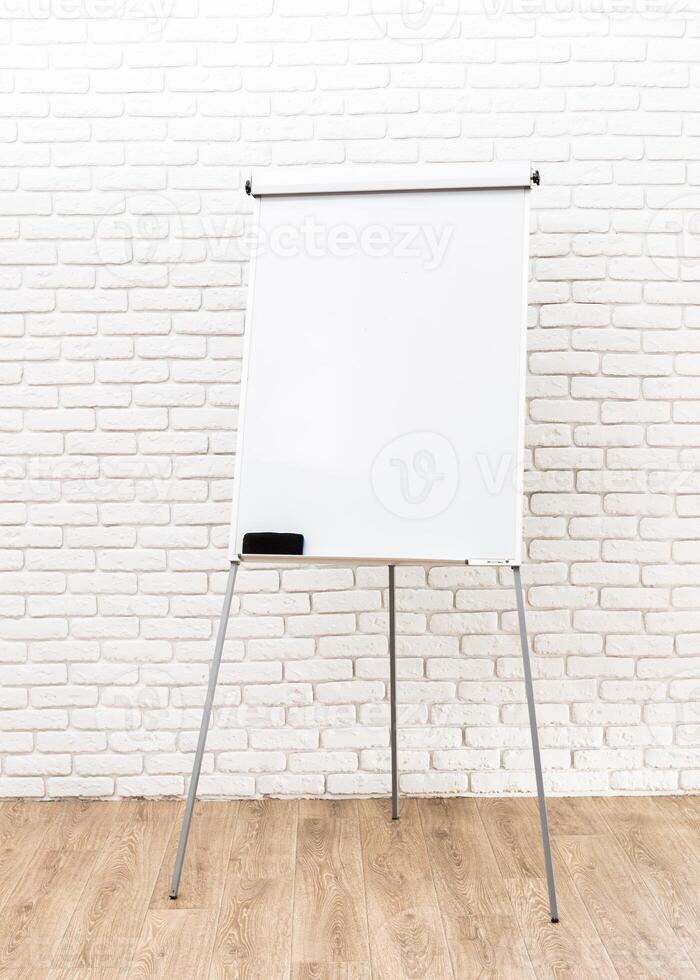 Blank whiteboard on a tripod stand against a textured brick wall in a well-lit room photo