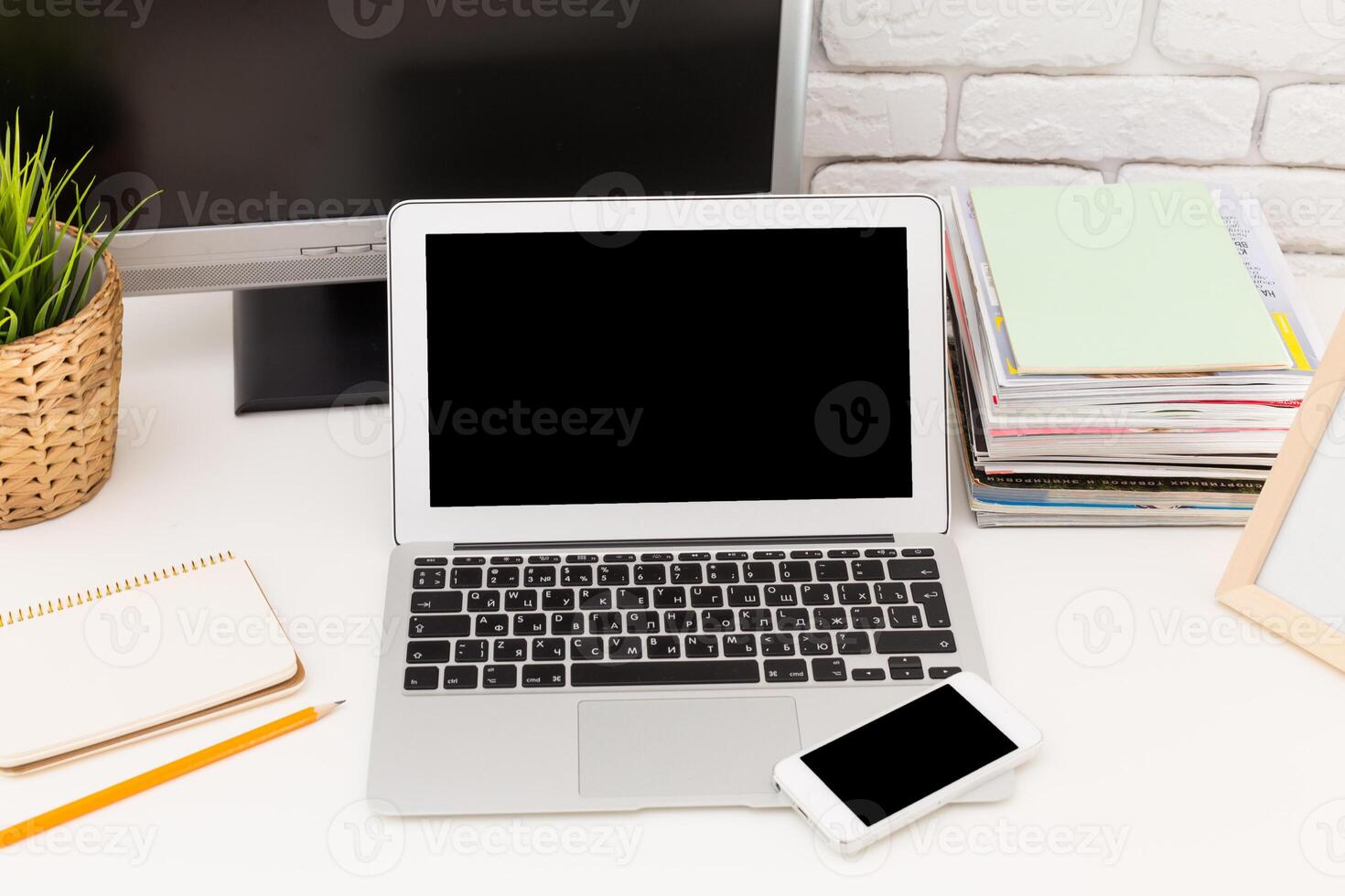 Workspace featuring a laptop and smartphone with notepad and magazines, set on a clean desk photo