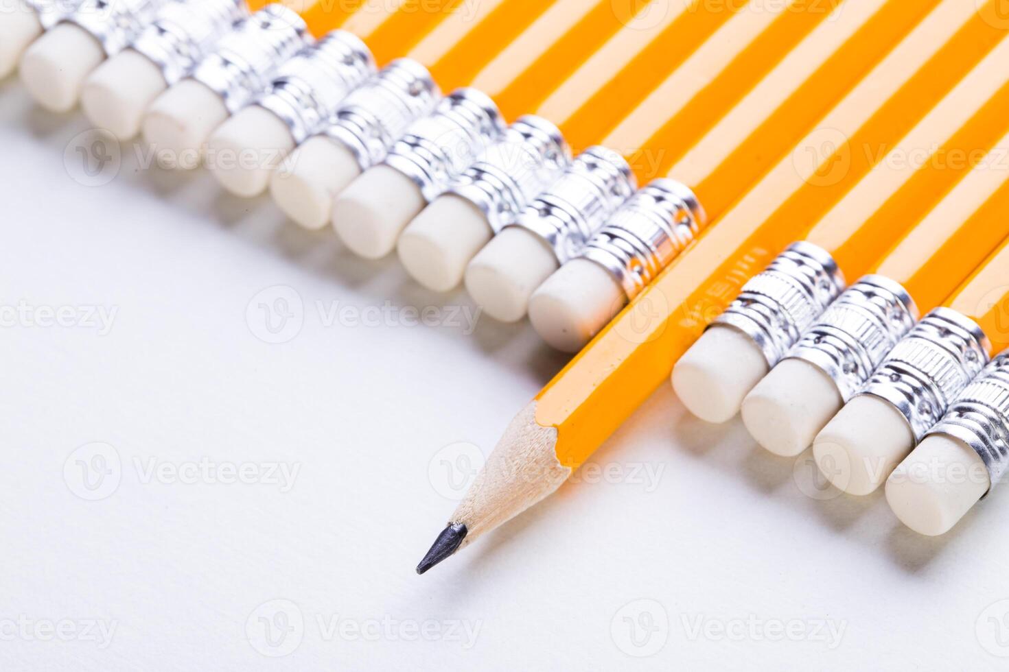 Numerous yellow pencils with erasers arranged neatly on a white surface photo