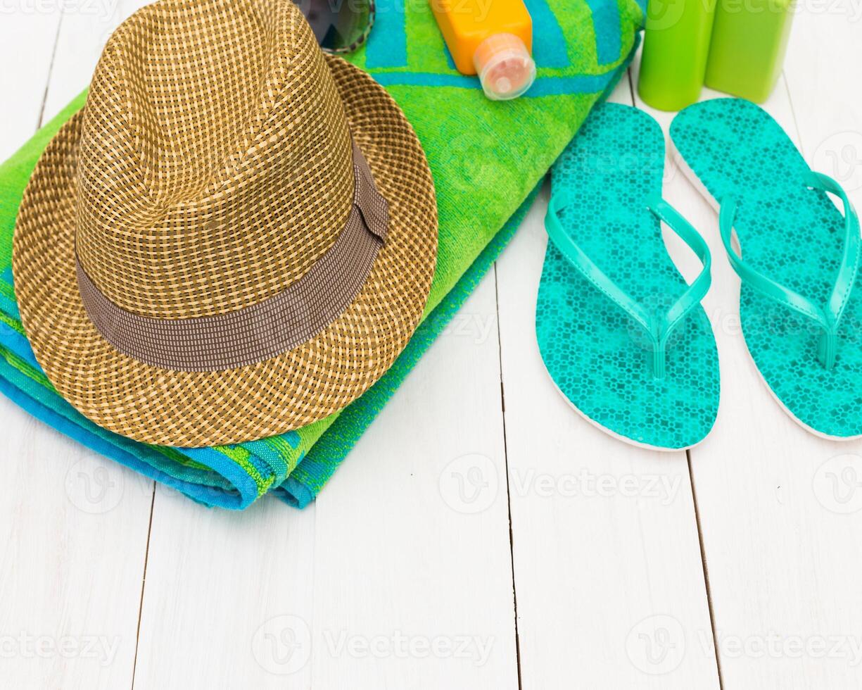 Summer beach essentials including towel, sun hat, sunscreen, and flip flops arranged on a bright wooden surface photo