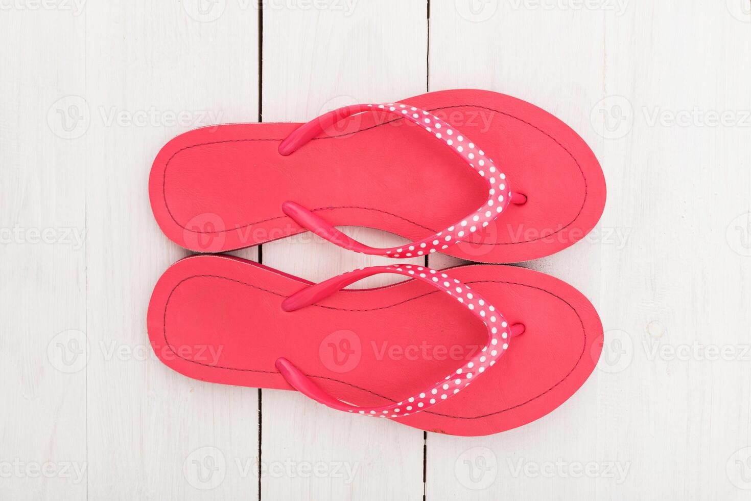 Bright pink flip-flops with white polka dots on a wooden surface, perfect for summer wear at the beach or poolside photo
