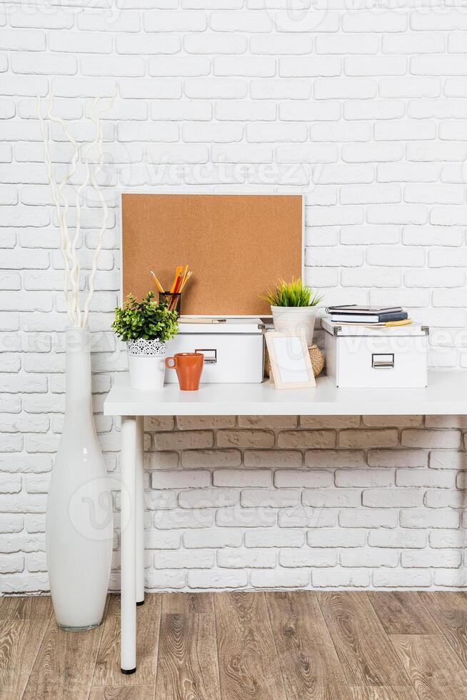 Organized workspace with plants and stationery on a desk against a brick wall backdrop photo