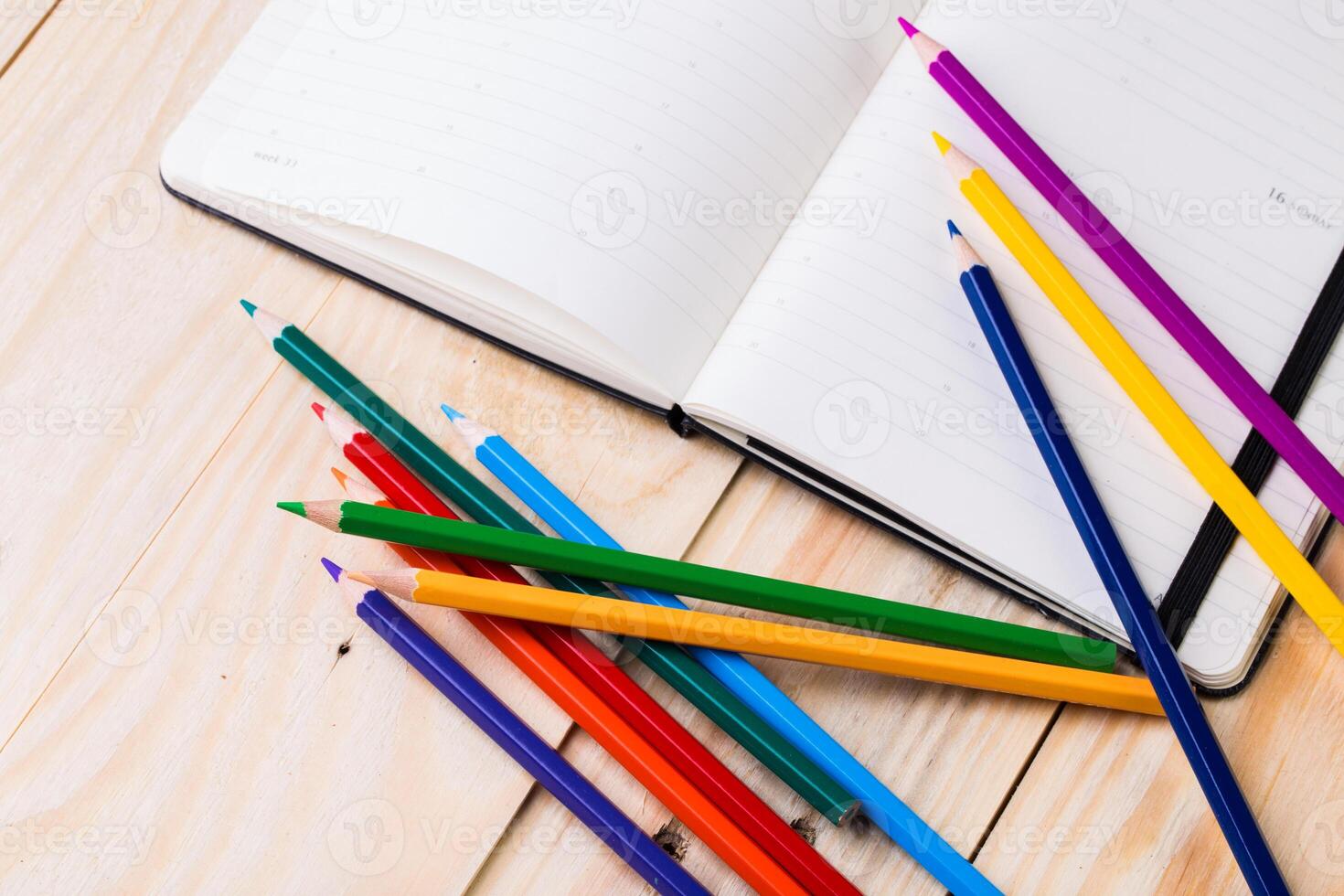 Colorful pencils scattered beside an open notebook on a wooden surface create a vibrant study space photo