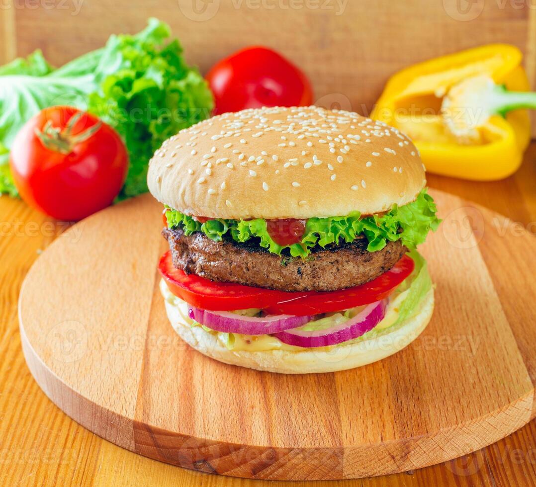 Juicy handmade burger topped with fresh vegetables served on a wooden board in natural light photo