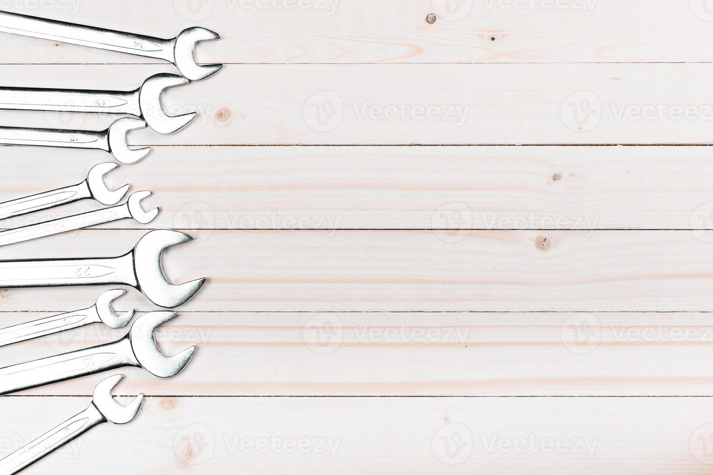 Collection of wrenches arranged on a wooden surface for mechanical and repair jobs in a workshop setting photo