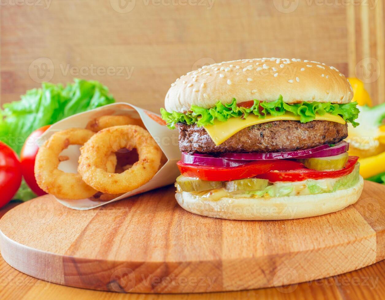Delicious cheeseburger with fresh vegetables and crispy onion rings on a wooden platter photo