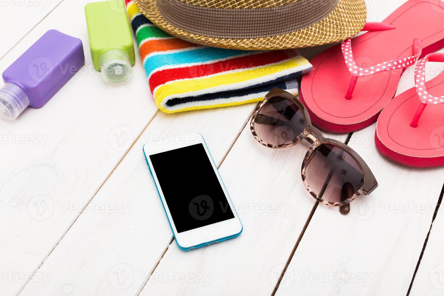 Bright summer essentials on a wooden surface including sunglasses, beach towel, sunscreen, sandals, and a smartphone for a fun day at the beach photo