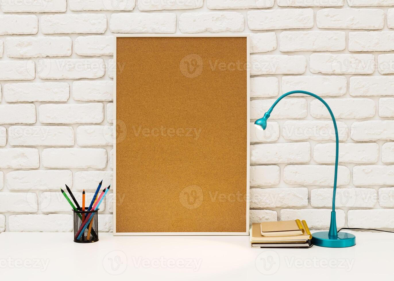 Workspace corner with blank cork board, desk lamp, and stationery items in a modern setting photo