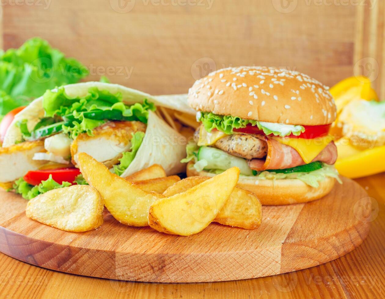 Delicious burger and chicken wrap served with golden fries on a wooden platter in a cozy setting photo