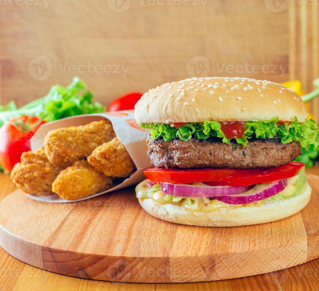 Delicious burger with fresh toppings alongside crispy chicken pieces on a wooden surface photo