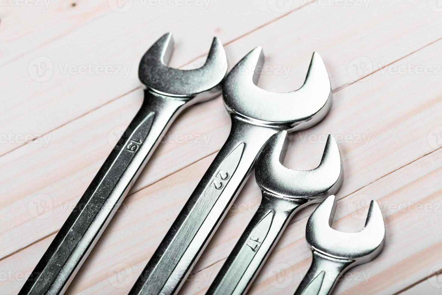 Set of four metal wrenches of varying sizes arranged neatly on a wooden surface during daytime photo