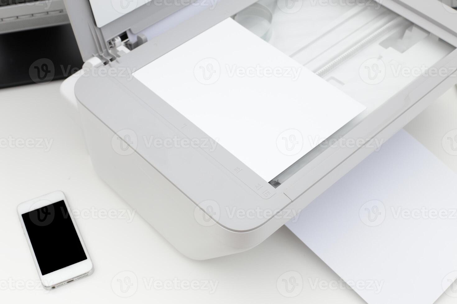 Printer in an office setting with blank paper and smartphone nearby during a workday routine photo